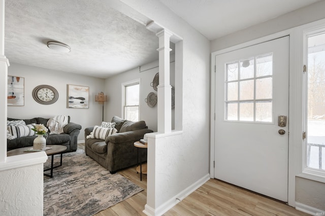 entryway with light hardwood / wood-style floors, a textured ceiling, and ornate columns