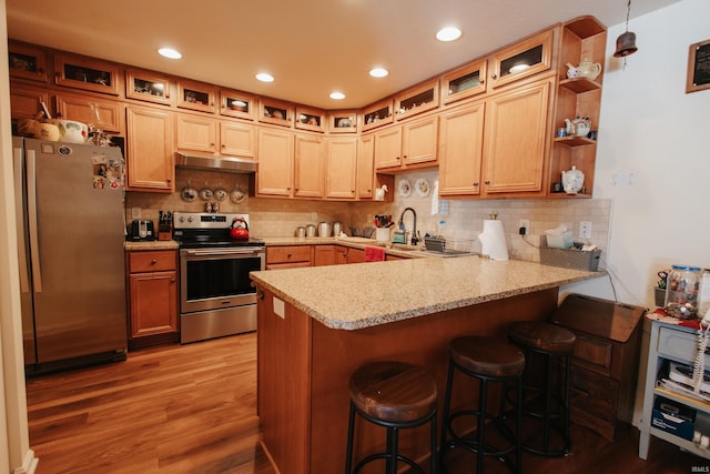 kitchen with light hardwood / wood-style floors, kitchen peninsula, stainless steel appliances, a kitchen breakfast bar, and light stone counters