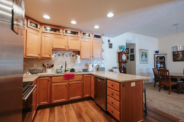 kitchen with kitchen peninsula, stainless steel appliances, tasteful backsplash, light wood-type flooring, and sink