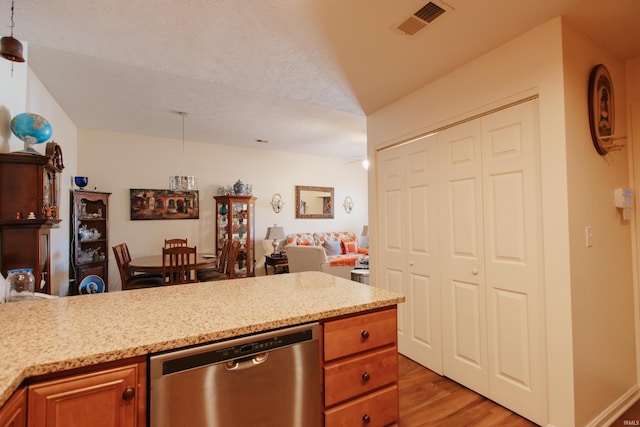 kitchen featuring light stone counters, hanging light fixtures, dishwasher, and light wood-type flooring