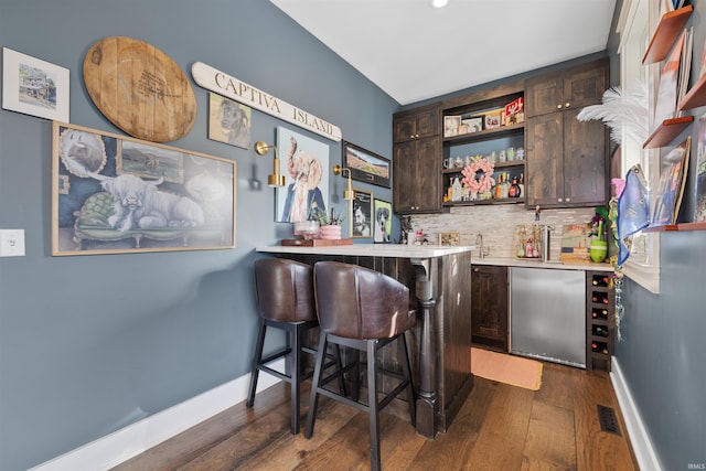 bar with dark hardwood / wood-style flooring, backsplash, dark brown cabinetry, and stainless steel refrigerator