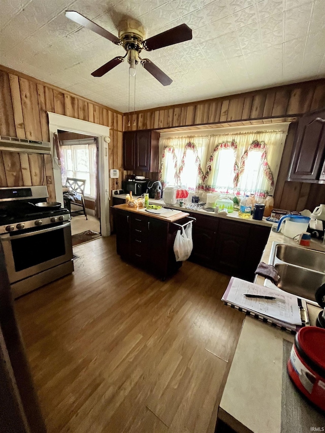 kitchen featuring wooden walls, dark brown cabinetry, and stainless steel gas range oven