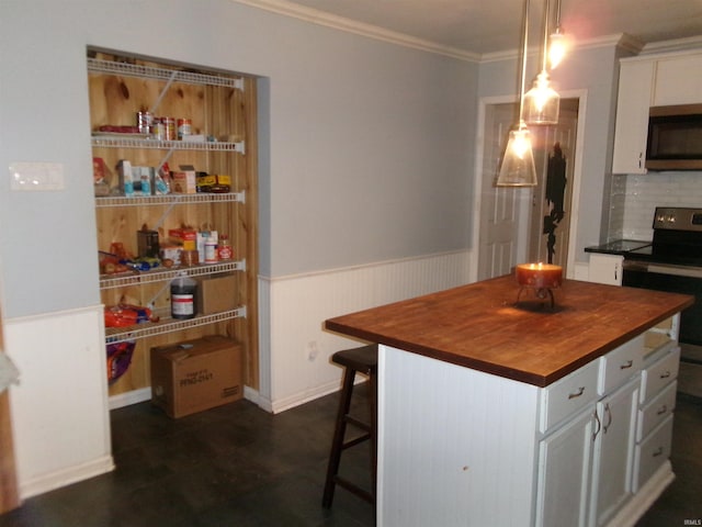 kitchen featuring appliances with stainless steel finishes, a kitchen island, decorative light fixtures, white cabinetry, and butcher block countertops