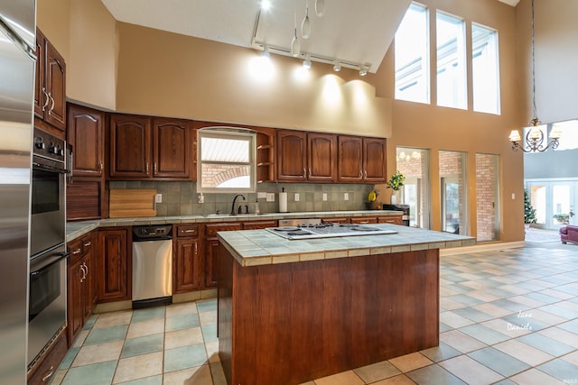 kitchen with a towering ceiling, decorative backsplash, tile countertops, and a kitchen island