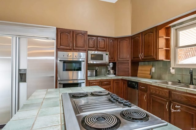 kitchen featuring tile countertops, decorative backsplash, stainless steel appliances, and sink