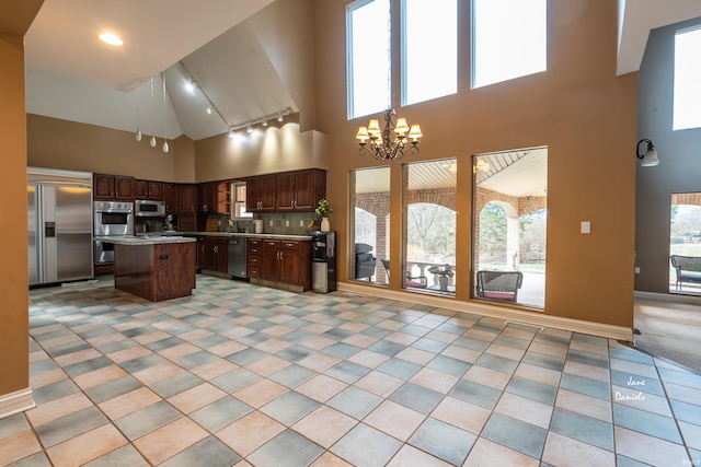 kitchen with a center island, decorative backsplash, a towering ceiling, appliances with stainless steel finishes, and a chandelier