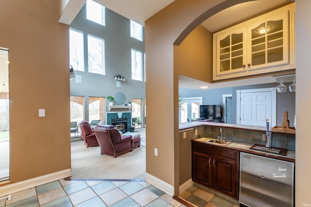 kitchen featuring dishwasher, tile countertops, sink, light tile patterned flooring, and a high ceiling