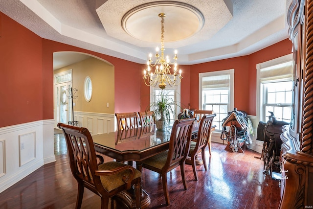 dining area with a raised ceiling, dark wood-type flooring, an inviting chandelier, and a textured ceiling