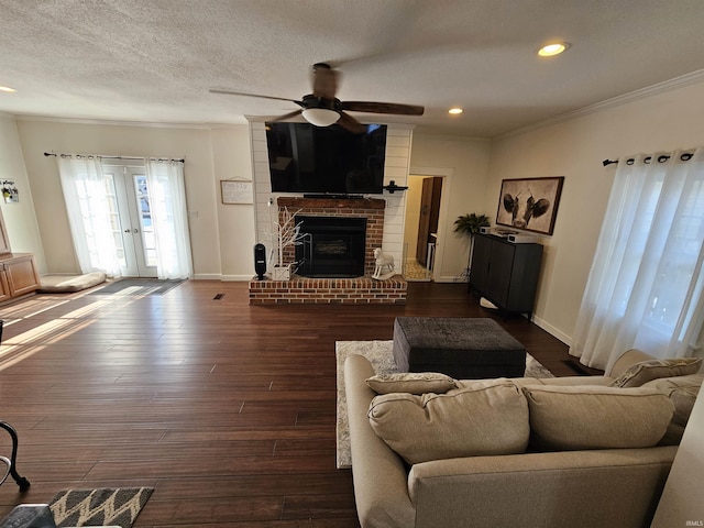 living room with a brick fireplace, dark hardwood / wood-style flooring, french doors, a textured ceiling, and ornamental molding