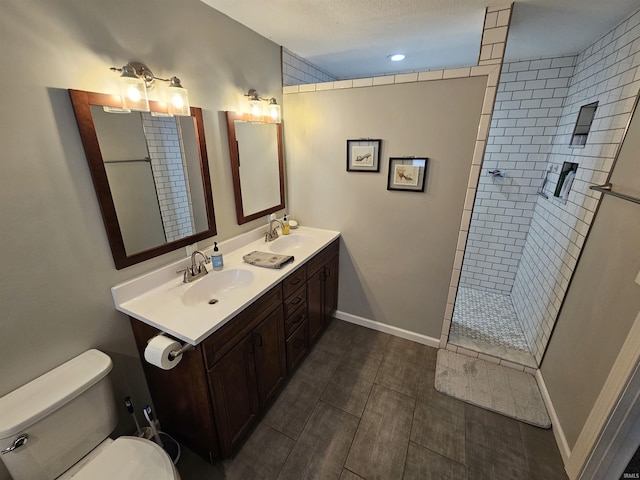 bathroom featuring a textured ceiling, tiled shower, vanity, and toilet