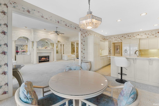 carpeted dining space featuring ornate columns, ceiling fan, crown molding, and sink