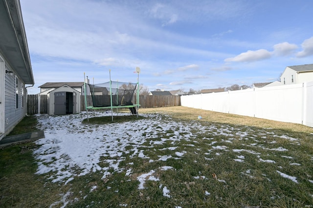 yard layered in snow featuring a storage shed and a trampoline