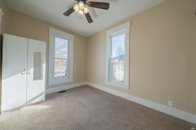 carpeted spare room with ceiling fan and plenty of natural light