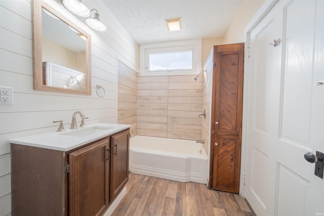 bathroom with vanity, tiled shower / bath, hardwood / wood-style floors, wooden walls, and a textured ceiling