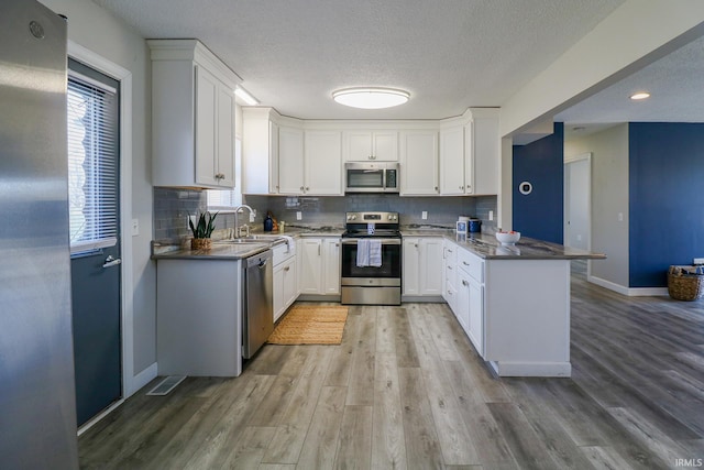 kitchen featuring white cabinetry, stainless steel appliances, tasteful backsplash, light hardwood / wood-style floors, and kitchen peninsula