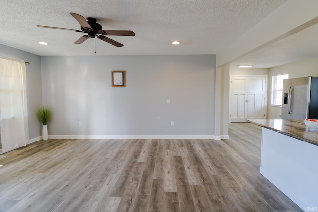 unfurnished living room featuring a textured ceiling, ceiling fan, and light hardwood / wood-style floors