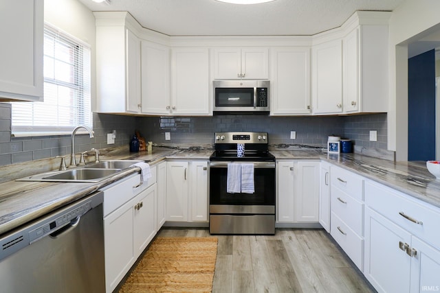 kitchen featuring white cabinets, appliances with stainless steel finishes, tasteful backsplash, sink, and light hardwood / wood-style flooring