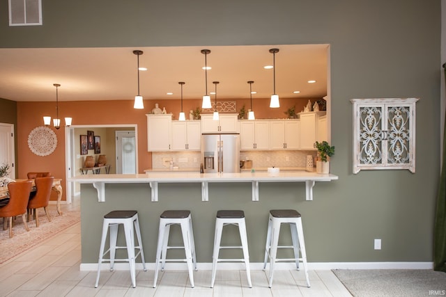 kitchen featuring decorative light fixtures, white cabinetry, backsplash, stainless steel fridge, and a breakfast bar