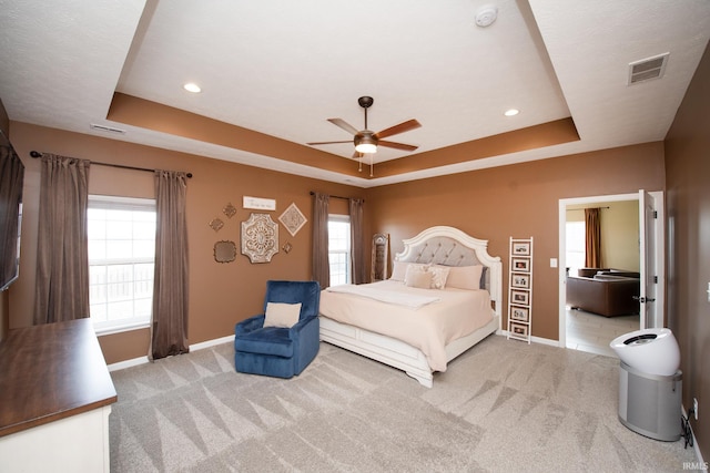 bedroom featuring ceiling fan, light carpet, and a tray ceiling