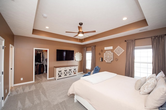 carpeted bedroom with ceiling fan, a walk in closet, and a raised ceiling