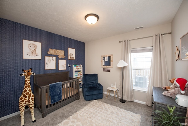 bedroom with a textured ceiling, a nursery area, and carpet floors