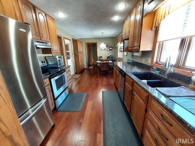 kitchen featuring sink, hanging light fixtures, stainless steel appliances, and dark stone countertops