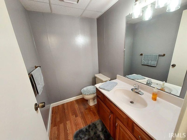 bathroom featuring toilet, vanity, wood-type flooring, and a drop ceiling