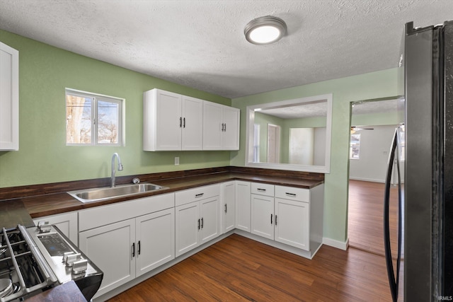 kitchen with sink, white cabinetry, butcher block counters, and black refrigerator