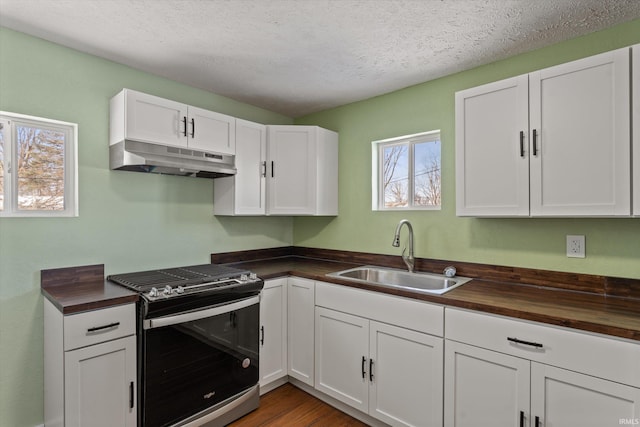 kitchen with a textured ceiling, stainless steel gas range, wood counters, white cabinetry, and sink