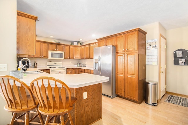 kitchen with a breakfast bar, light wood-type flooring, white appliances, and kitchen peninsula