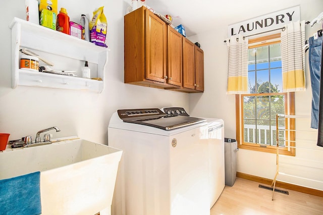 clothes washing area with cabinets, washing machine and dryer, sink, and light hardwood / wood-style flooring