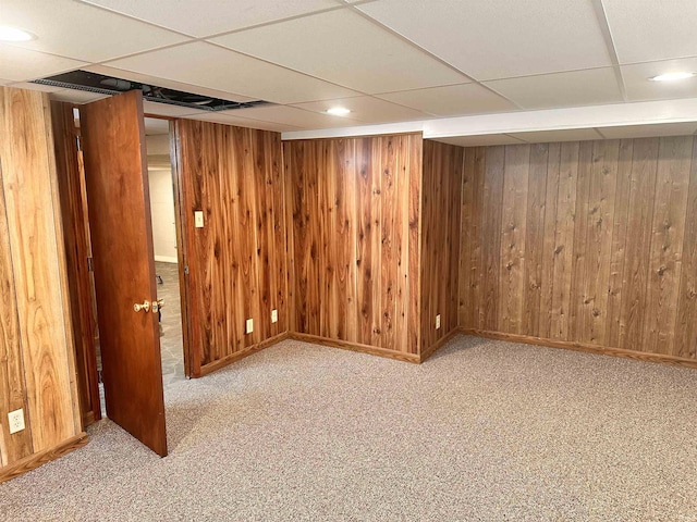 basement with wood walls, light colored carpet, and a drop ceiling