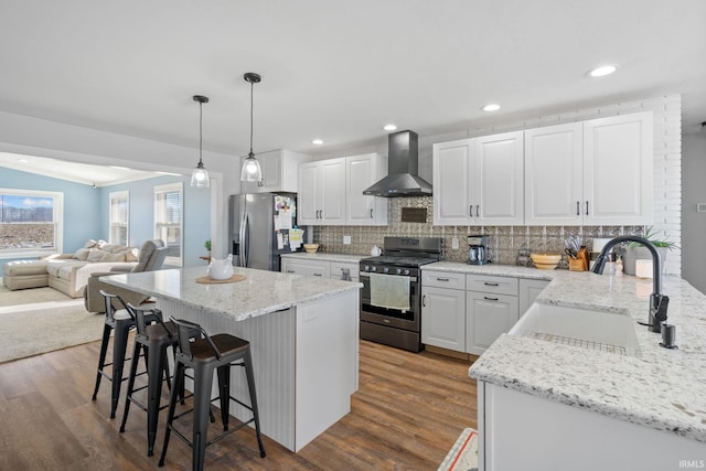 kitchen featuring white cabinetry, decorative light fixtures, wall chimney range hood, and appliances with stainless steel finishes