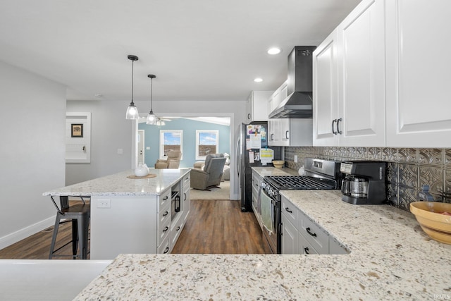 kitchen featuring white cabinetry, appliances with stainless steel finishes, backsplash, hanging light fixtures, and wall chimney range hood