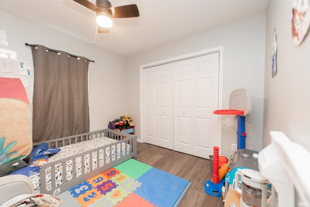 bedroom with ceiling fan, wood-type flooring, a nursery area, and a closet