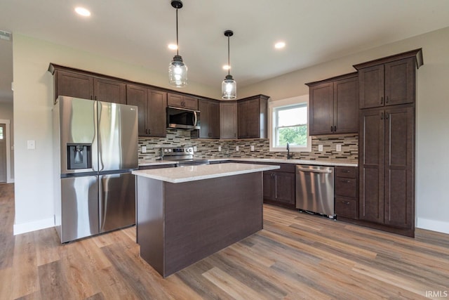 kitchen with stainless steel appliances, dark brown cabinetry, hanging light fixtures, and light hardwood / wood-style floors