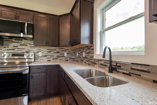 kitchen with sink, stainless steel appliances, dark brown cabinets, and light stone counters