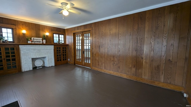 unfurnished living room with a healthy amount of sunlight, wooden walls, a brick fireplace, and french doors