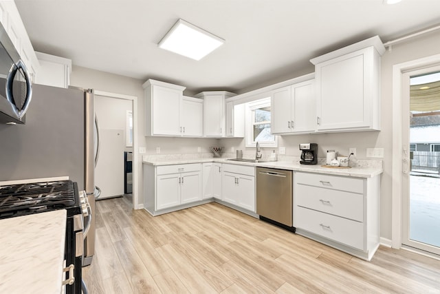 kitchen featuring light stone countertops, light hardwood / wood-style floors, white cabinetry, sink, and stainless steel appliances