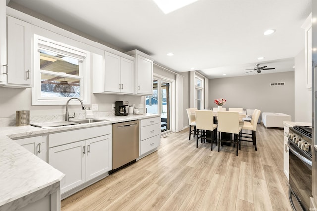 kitchen with appliances with stainless steel finishes, white cabinetry, sink, light stone counters, and light hardwood / wood-style flooring