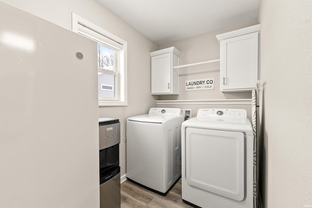 clothes washing area featuring cabinets, separate washer and dryer, and light hardwood / wood-style floors