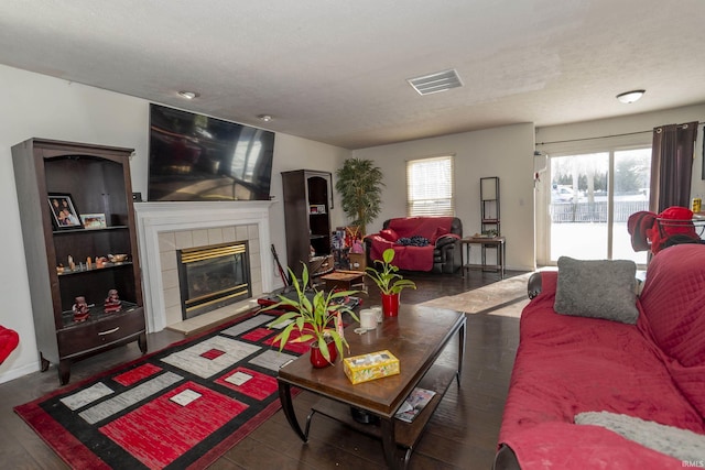 living room featuring a tiled fireplace, dark wood-type flooring, and a textured ceiling