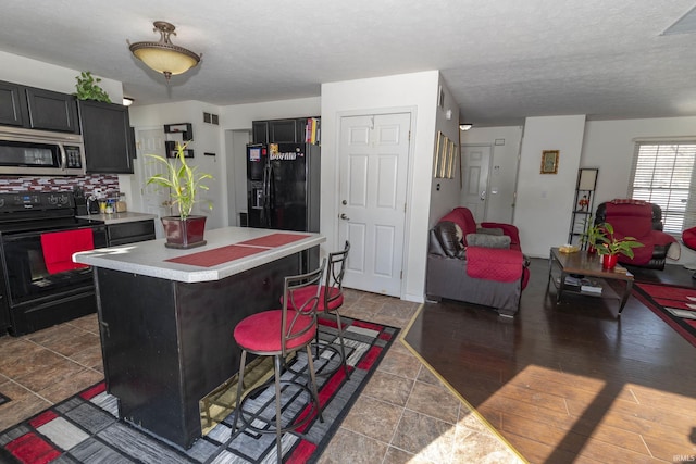 kitchen featuring a kitchen bar, a textured ceiling, black appliances, and a center island