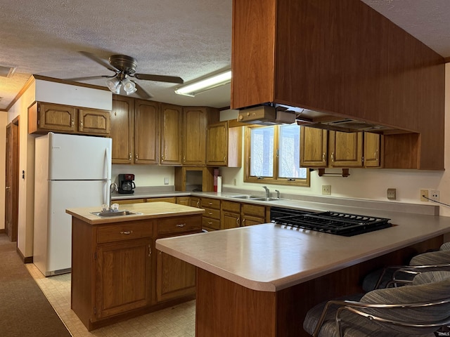 kitchen featuring ceiling fan, sink, white refrigerator, a textured ceiling, and a center island