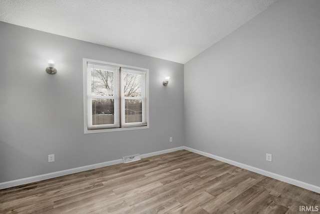 unfurnished room with light hardwood / wood-style floors, a textured ceiling, and lofted ceiling