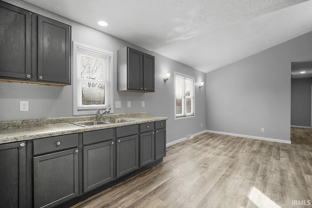 kitchen featuring hardwood / wood-style floors, a textured ceiling, gray cabinetry, sink, and vaulted ceiling