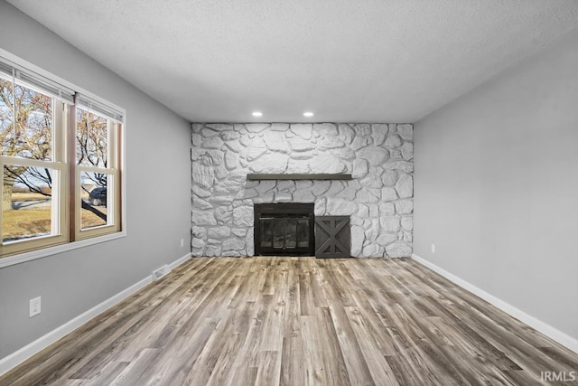 unfurnished living room featuring wood-type flooring, a textured ceiling, and a stone fireplace