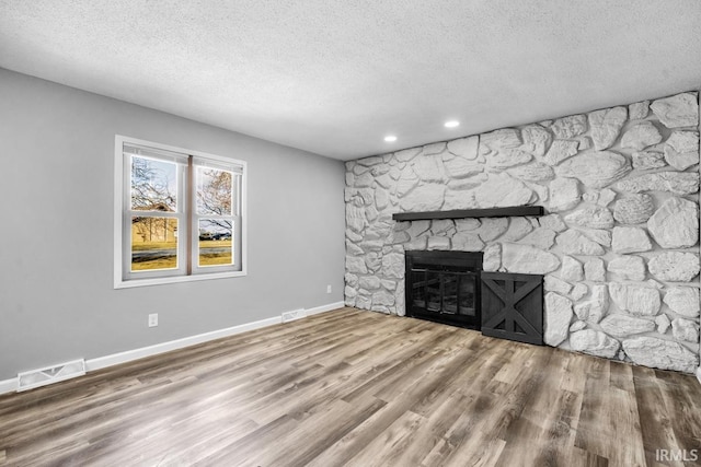 unfurnished living room with a textured ceiling, hardwood / wood-style floors, and a stone fireplace