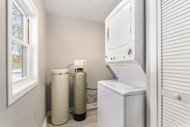 clothes washing area with stacked washer / dryer, light wood-type flooring, a wealth of natural light, and a textured ceiling