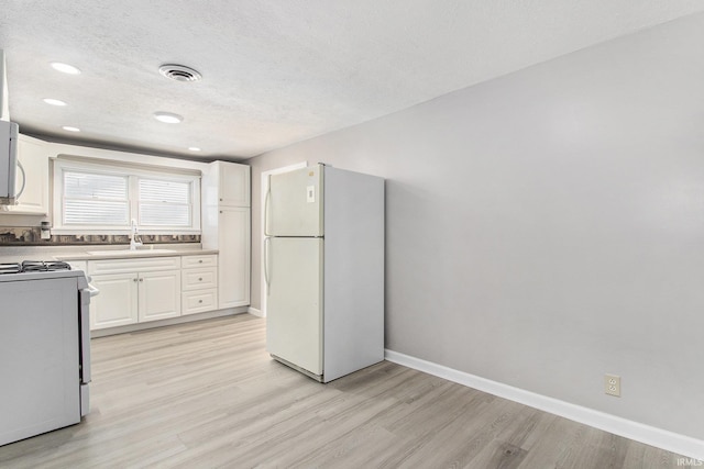 kitchen with white appliances, a textured ceiling, white cabinetry, sink, and light hardwood / wood-style flooring